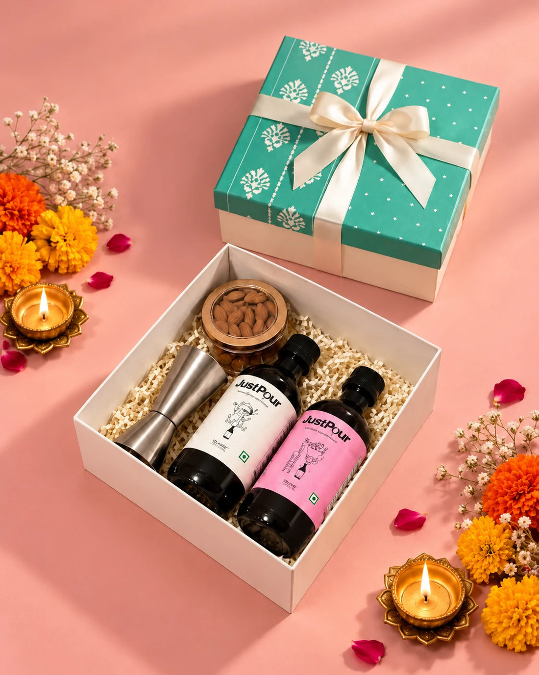 JustPour Diwali Gift Box with a cream ribbon beside the open box, surrounded by marigolds and diyas